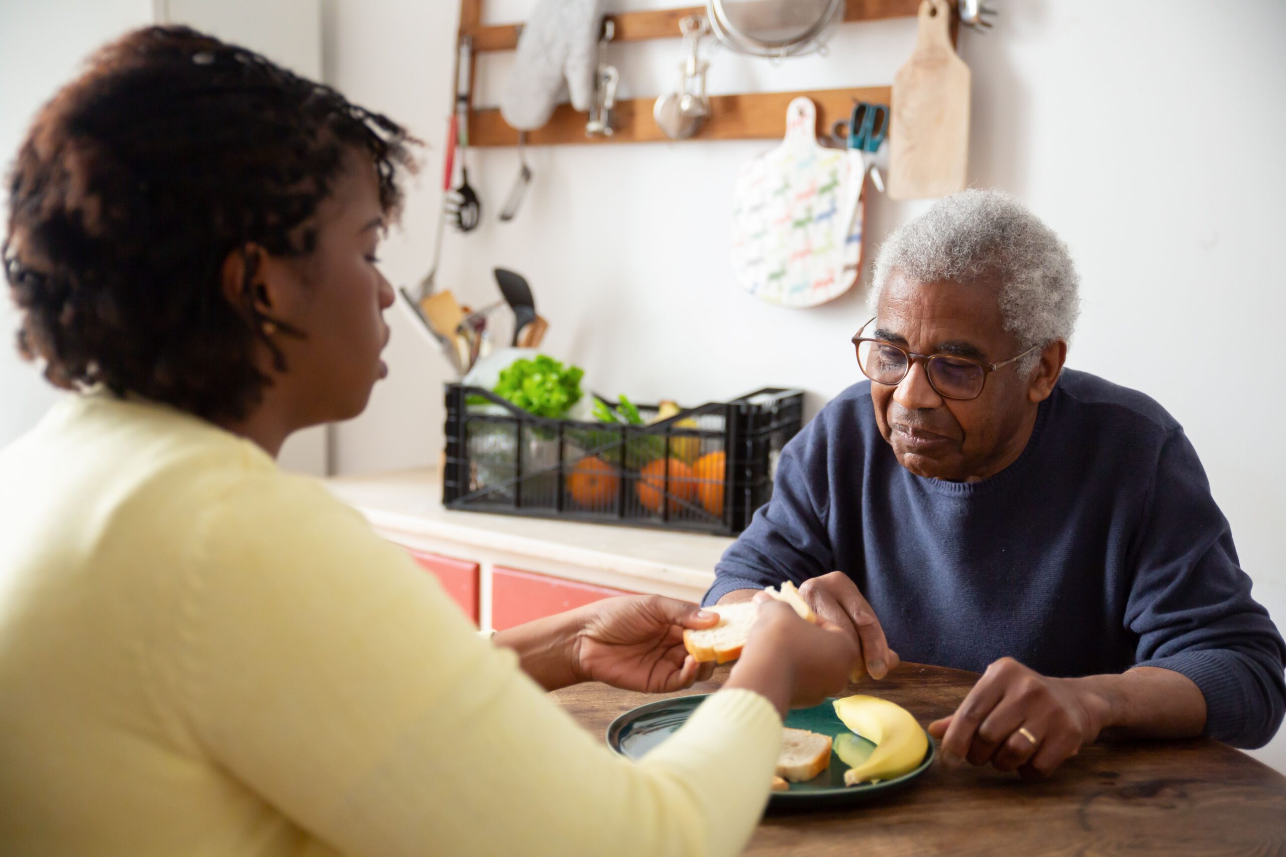 Adult daughter gently holding hands and talking with her aging mother in a sunlit living room, sharing a warm and supportive caregiving moment